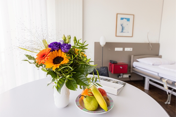 Eine Obstschale und Blumen auf dem Tisch eines Patientenzimmers.