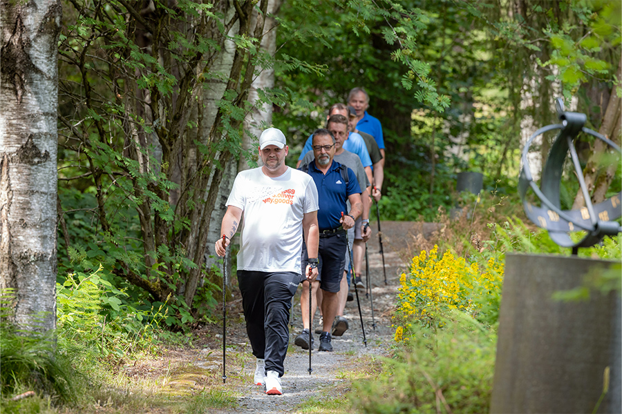 Eine Gruppe von Männern mit Walking-Stöcken läuft im Wald einen Pfad entlang.