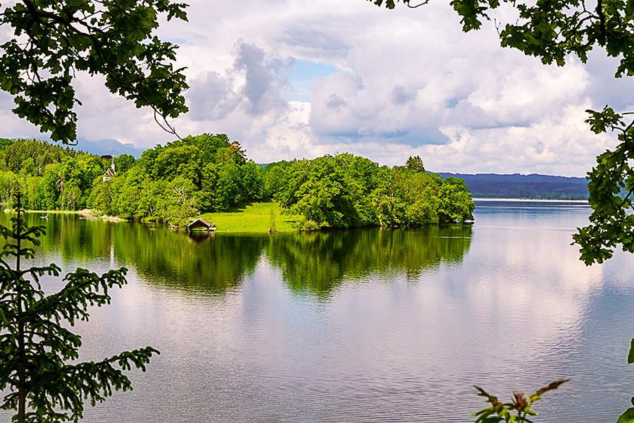 Das Panorama eines Sees, im Hintergrund sehen wir grüne Bäume am Ufer.