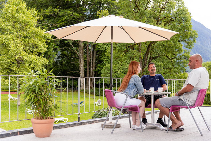 Zwei Männer und eine Frau sitzen um einen Tisch auf der Terrasse der Klinik. Zwei Männer und eine Frau sitzen um einen Tisch auf der Terrasse der Klinik.