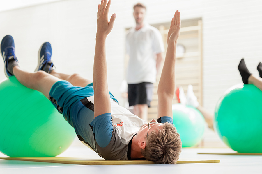 Ein Patient liegt mit den Beinen auf einem Gymnastikball auf dem Boden. Ein Patient liegt mit den Beinen auf einem Gymnastikball auf dem Boden.