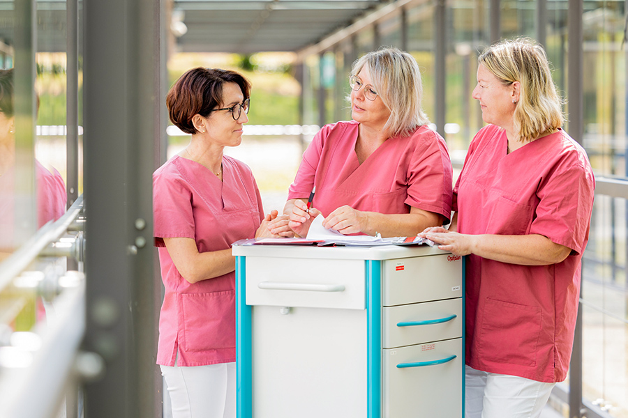 Drei Mitarbeiterinnen des Pflegepersonals unterhalten sich über eine Patientenakte.